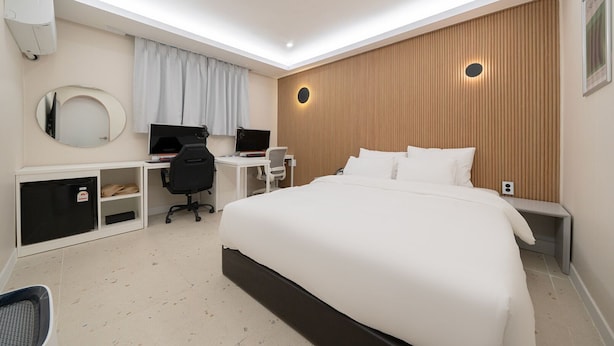 Ett modernt hotellrum med en stor säng, ett skrivbord med två datorskärmar, en stol och en garderob.