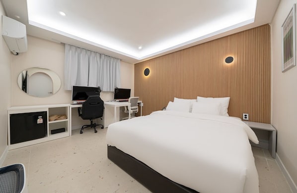 Een moderne hotelkamer met een groot bed, een bureau met twee monitoren, een stoel en een kledingkast.