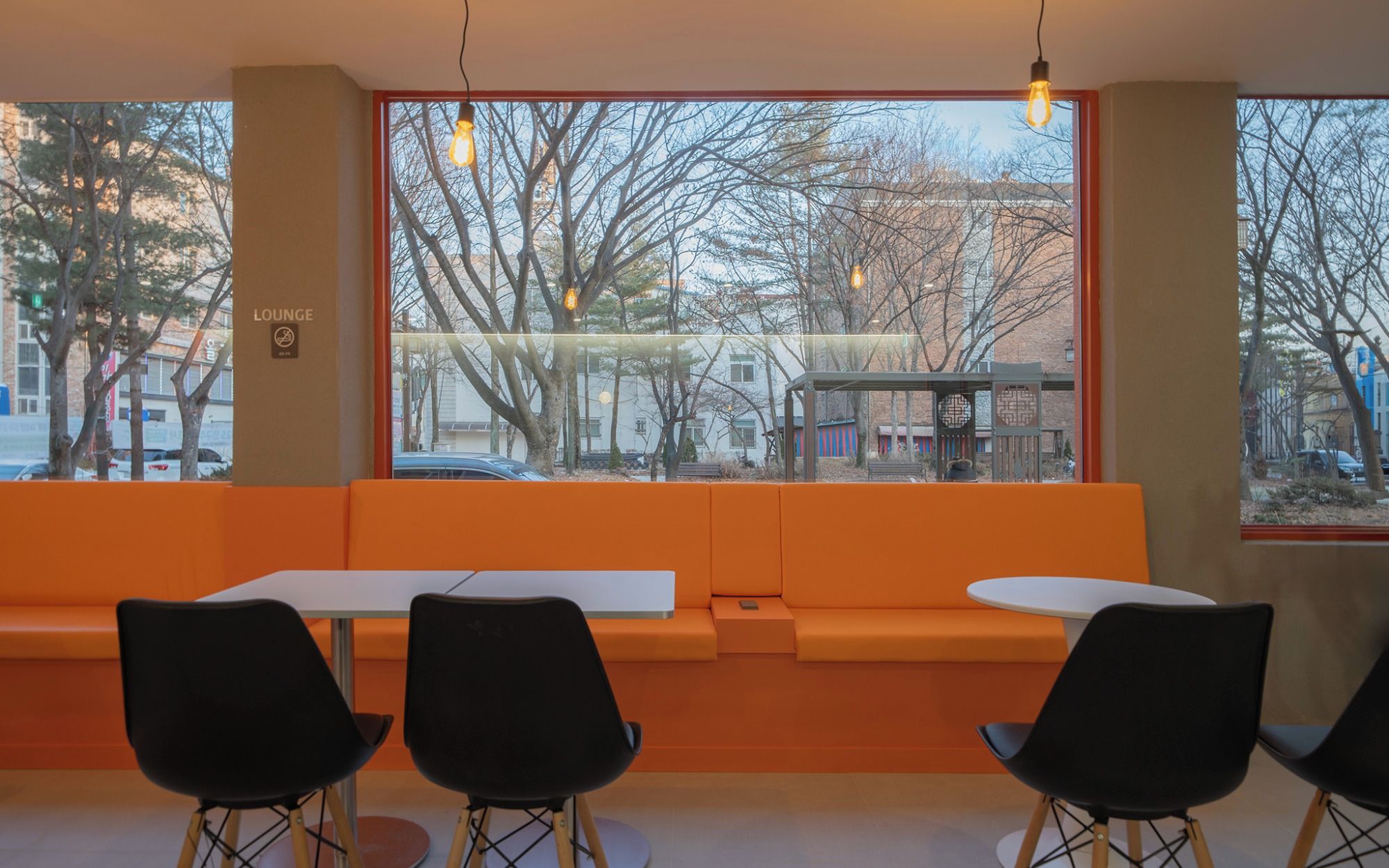 A seating area with orange cushions, black chairs, and a view of the street through large windows.
