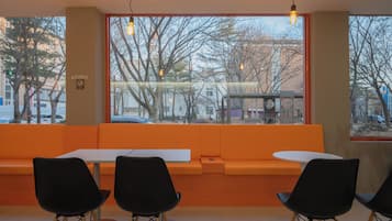 A seating area with orange cushions, black chairs, and a view of the street through large windows.