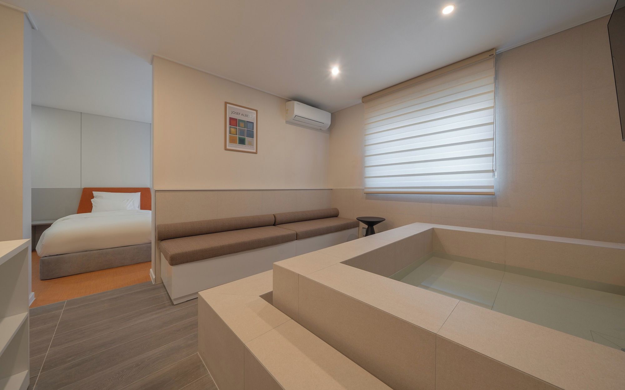 A modern hotel room with a bed, a seating area, a small table, and a bathtub.