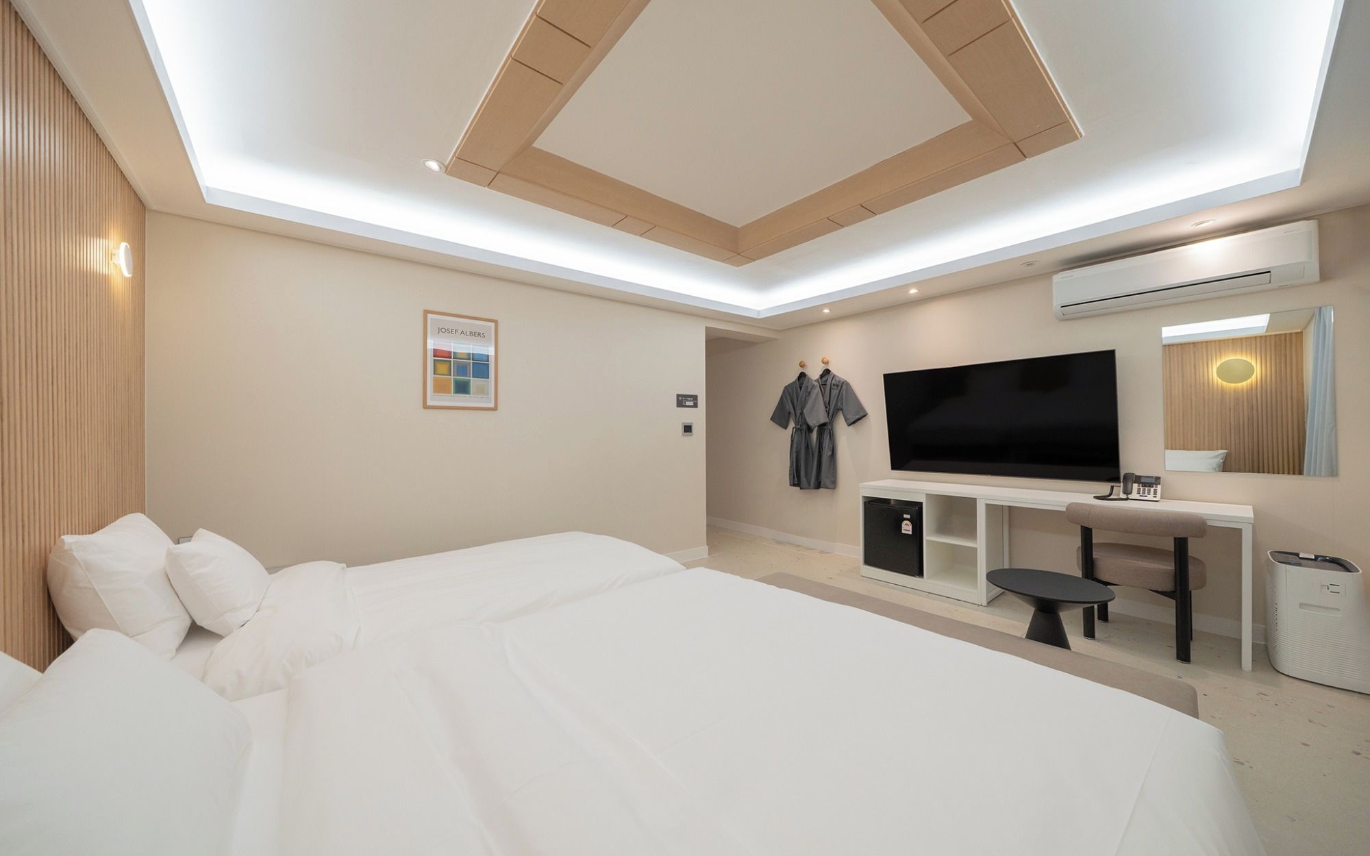 Una habitación de hotel moderna con una cama grande, un televisor de pantalla plana, un escritorio con silla y un espejo.