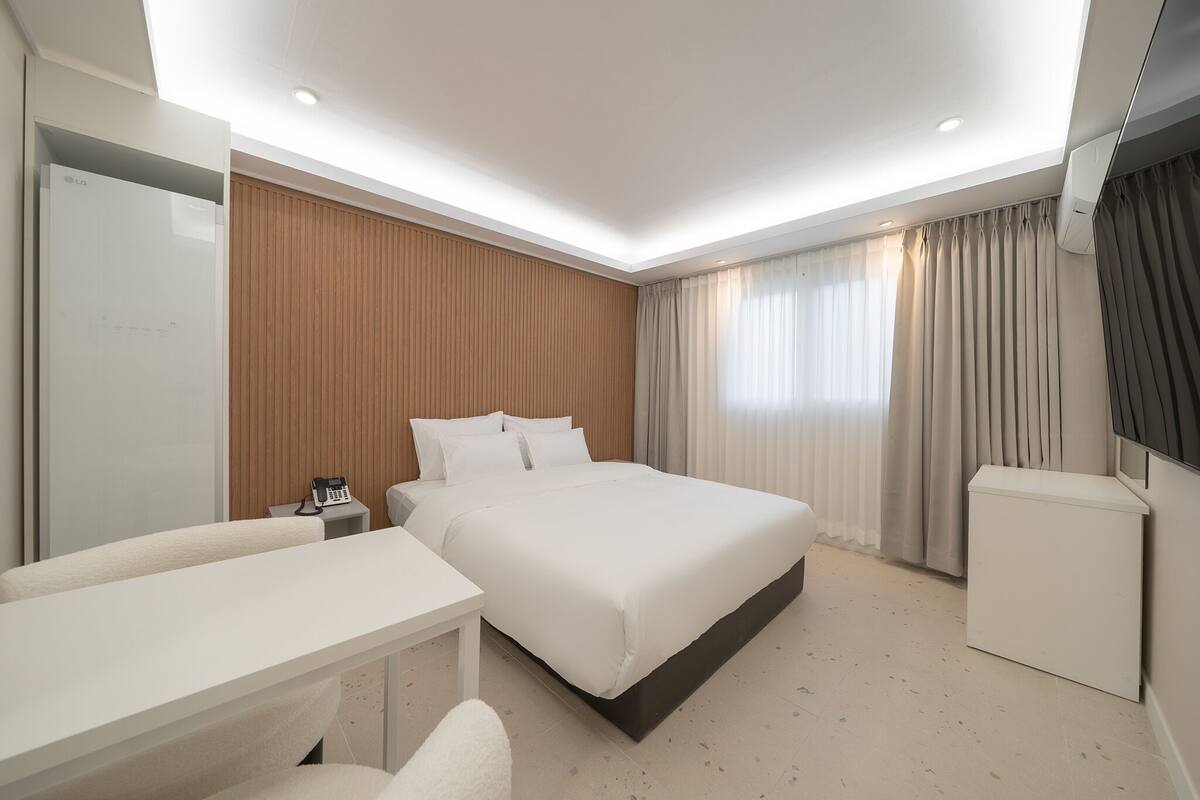 Una habitación de hotel con cama, escritorio, silla, armario y un pequeño mueble.