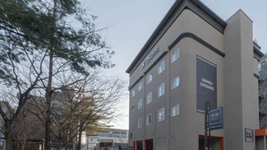 En modern hotellbyggnad med många fönster, en framträdande skylt som visar att hotellet snart öppnar och en parkeringsskylt.