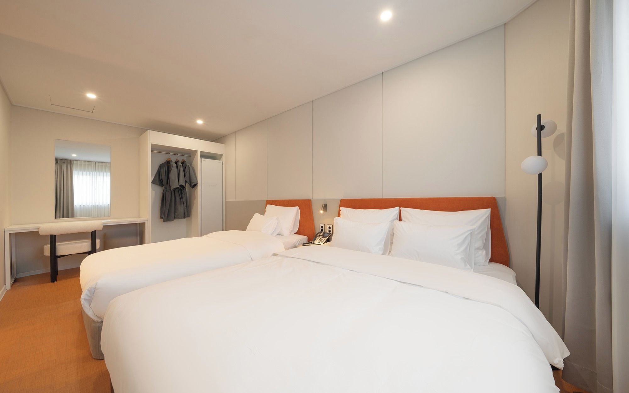 A hotel room with two beds, a bedside table, a mirror, a wardrobe, and a phone.