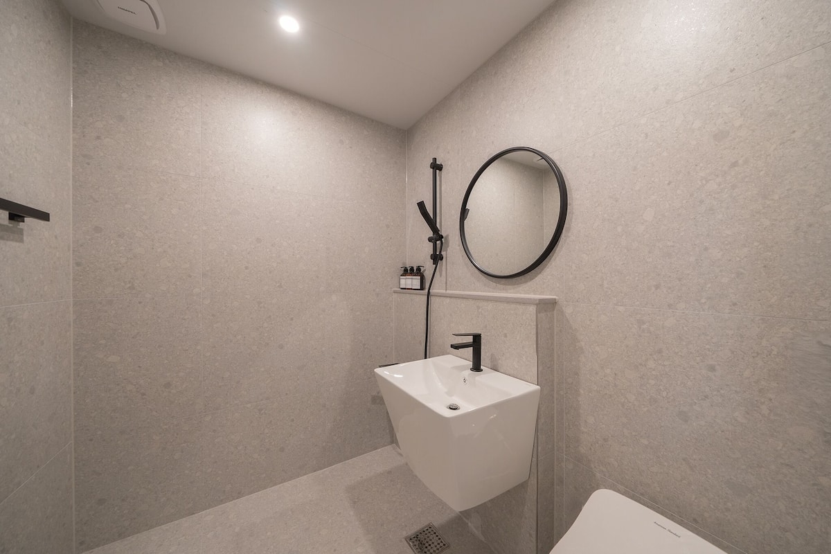 Un baño moderno con lavamanos independiente, ducha de mano y espejo redondo.