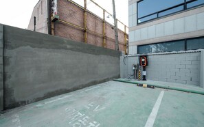 Un estacionamiento con un muro de concreto, un edificio de ladrillo y un edificio moderno con amplios ventanales.