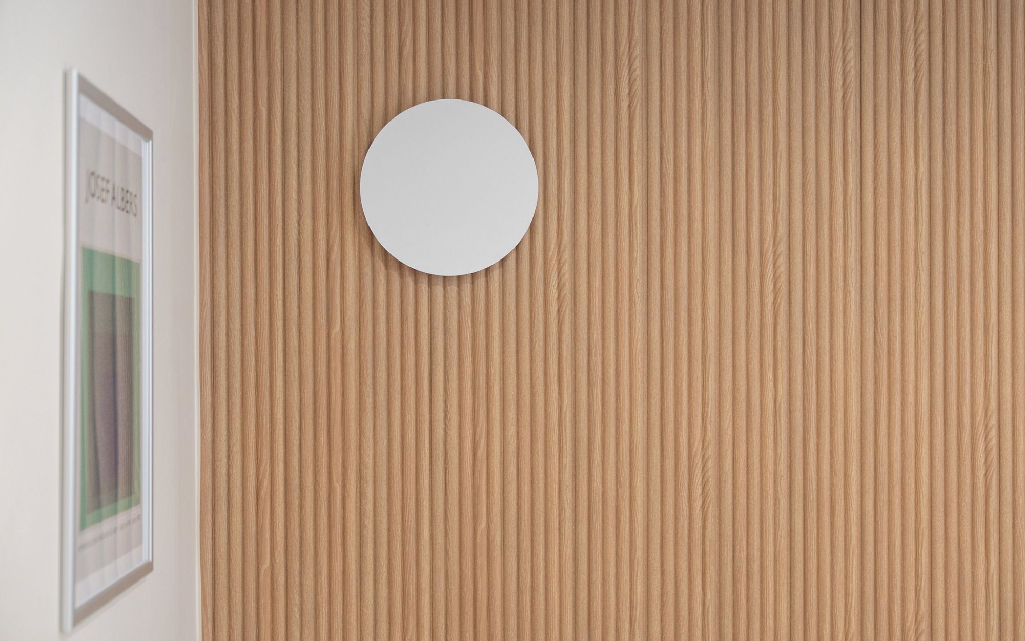 A wall with a vertical wood panel design and a round mirror centered on it.