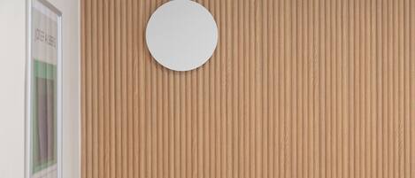 A wall with a vertical wood panel design and a round mirror centered on it.