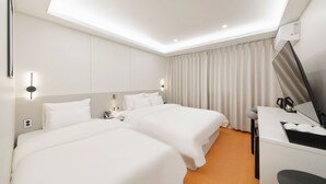 Ett hotellrum med två sängar, ett skrivbord, en stol, en spegel och ett fönster med gardiner.