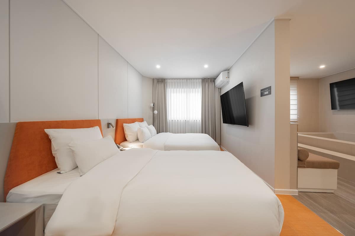 Habitación de hotel con dos camas, un televisor en la pared y una ventana con cortinas.