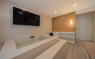Un baño moderno con una bañera grande, un televisor montado y un revestimiento de pared de madera.