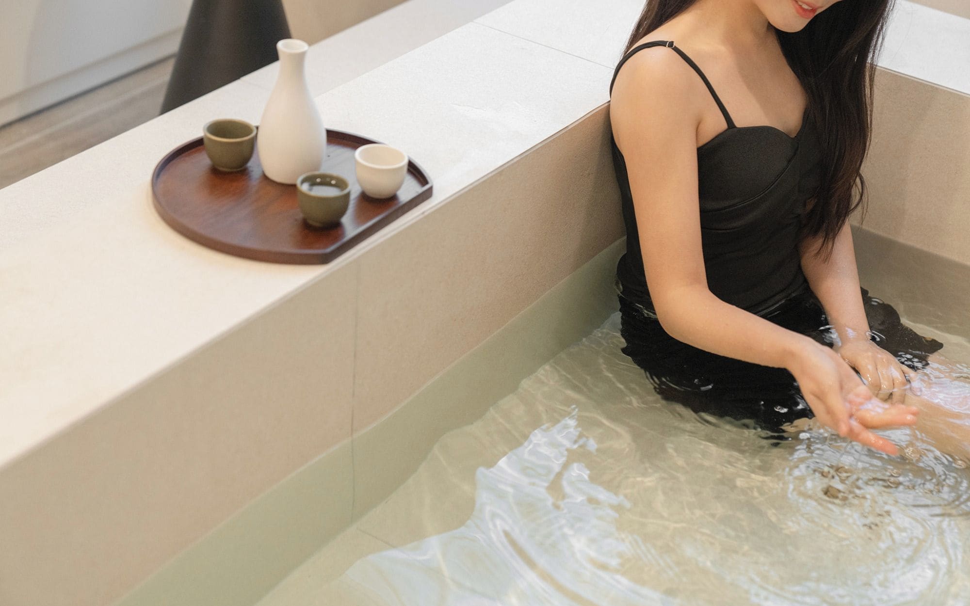 A person sitting in a bathtub with a tray of items on the edge.