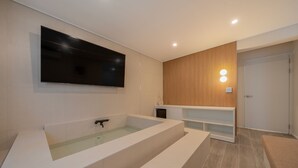 A modern bathroom with a large bathtub, a mounted TV, and built-in shelves.