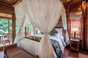 A room with a bed under a canopy, a nightstand with a lamp, and a view of greenery outside. - The Compass Rose Ubud (Ubud)