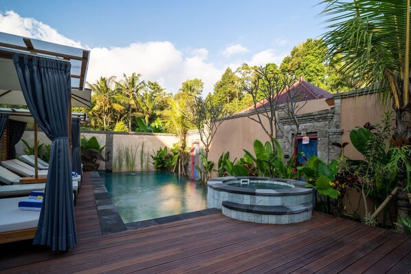 A pool area with lounge chairs, a hot tub, and lush tropical plants. - The Compass Rose Ubud (Ubud)