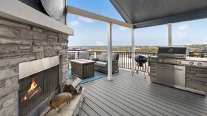 A covered outdoor patio with a stone fireplace, a grill, and outdoor furniture. - Bluemoon Retreat - Tiny Home 115 (Fredericksburg)