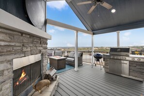 Eine überdachte Terrasse im Freien mit Kamin aus Stein, Grill und Gartenmöbeln.