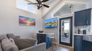 A modern kitchen with dark cabinets, a bar area, and a large TV. - Bluemoon Retreat - Tiny Home 115 (Fredericksburg)
