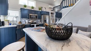 A modern kitchen with dark blue cabinets, a marble countertop, and a wicker basket with wine glasses. - Bluemoon Retreat - Tiny Home 115 (Fredericksburg)