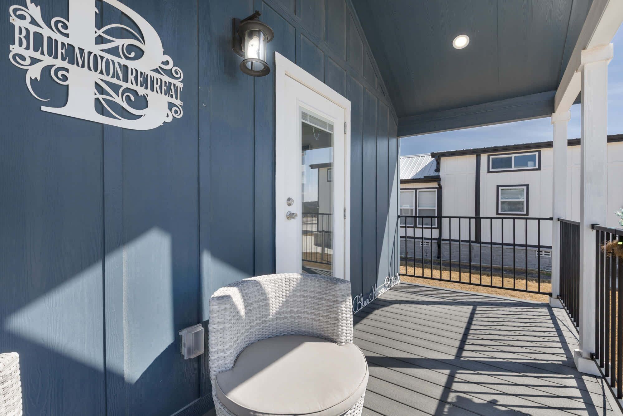 A covered outdoor area with a wicker chair, a wall sign, and a railing.