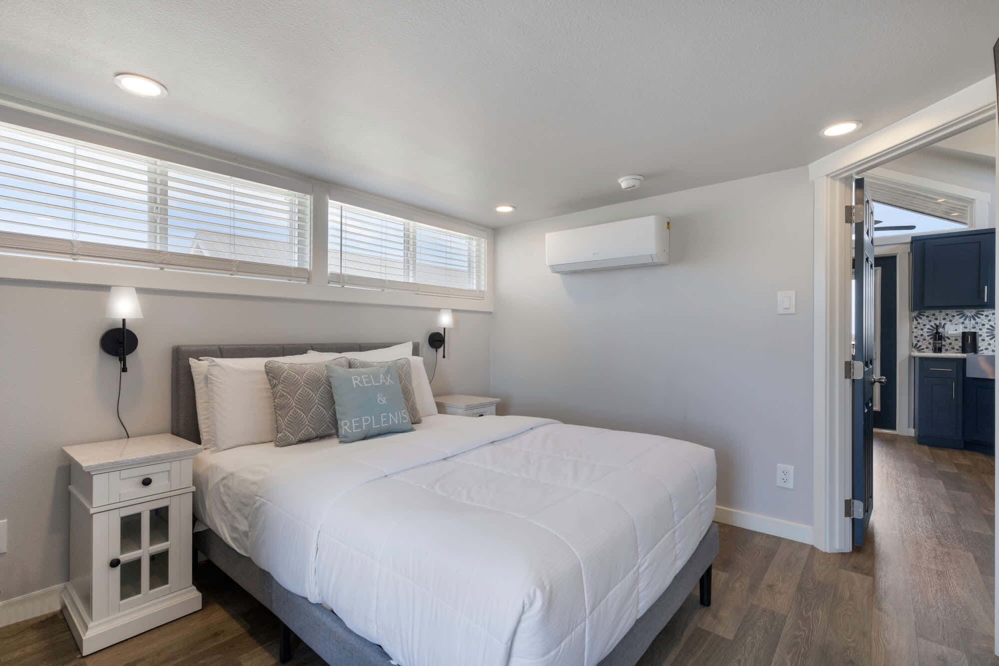 A bedroom with a bed, bedside tables, a wall-mounted air conditioner, and a window with blinds.