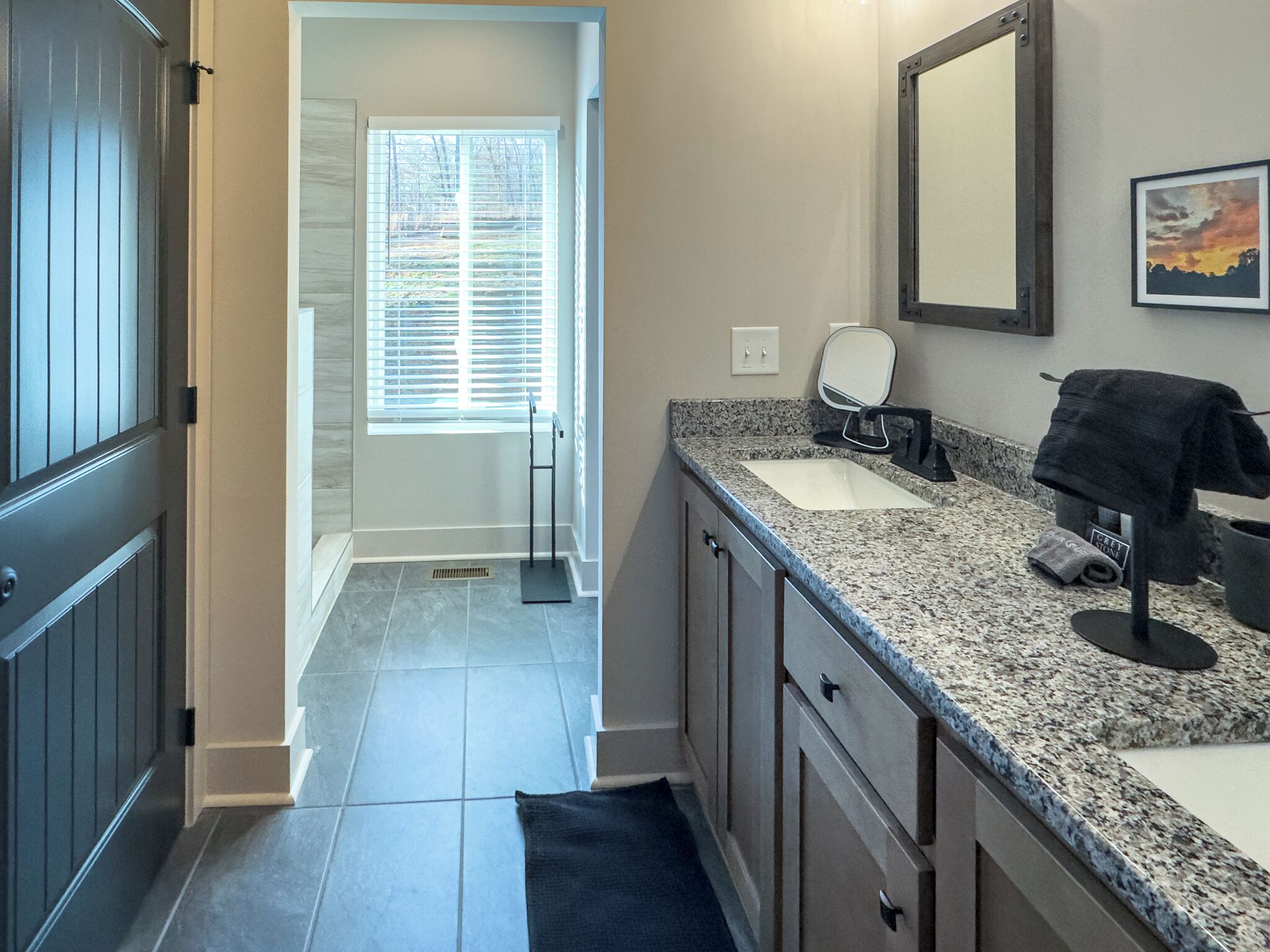 Un baño moderno con encimera de granito, un lavabo, un espejo y un perchero para toallas.