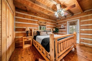 A log cabin bedroom with a wooden bed, a nightstand, a lamp, and a ceiling fan. - The Gathering in Blue Ridge (Blue Ridge)