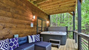 A wooden deck with a hot tub, a sofa with patterned cushions, and a sign indicating spa rules. - Knotty by Nature | Cherry Log Mountain Cabin (Blue Ridge)
