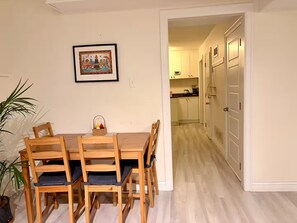 A dining area with a wooden table and chairs, a framed picture on the wall, and a potted plant. - Entire guest suite in Delta, Canada, Cozy & Stylish 1BR Perfect for Getaways (Delta)