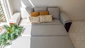 Ein modernes Wohnzimmer mit Schlafsofa, Topfpflanze und einem gerahmten abstrakten Kunstwerk an der Wand.