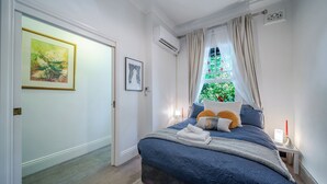 Ein Schlafzimmer mit einem großen Bett, einem Nachttisch mit Lampe und einem Fenster mit Vorhängen.