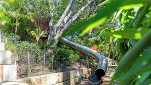 Eine gebogene Metallkonstruktion in einem Garten mit dichtem Grün und einem Holzzaun.