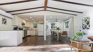 Una cocina moderna con armarios blancos, un comedor con mesa y sillas de madera, y un ventanal con cortinas.