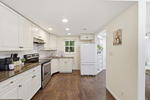 A modern kitchen with white cabinets, stainless steel appliances, and a wooden floor.