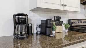Una cocina con cafetera, balanza, planta y bloque de cuchillos.
