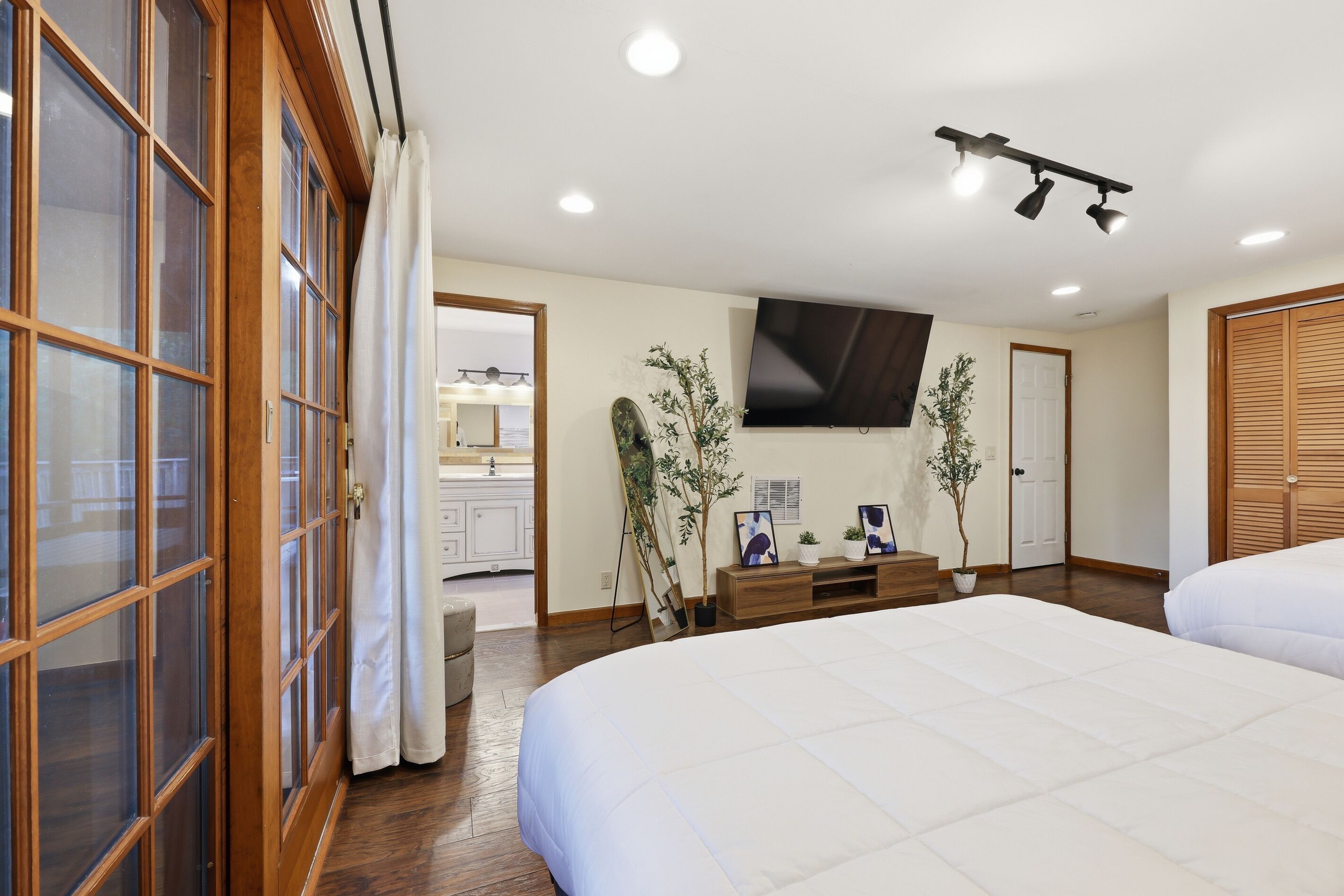 A bedroom with a large bed, wooden wardrobe, TV, and potted plants.