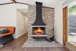 A fireplace with a stone facade, a wooden bench, and a view through a glass door.