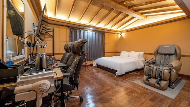 Ein Hotelzimmer mit Bett, Massagesessel, Schreibtisch mit Kopfhörern und Spiegel.