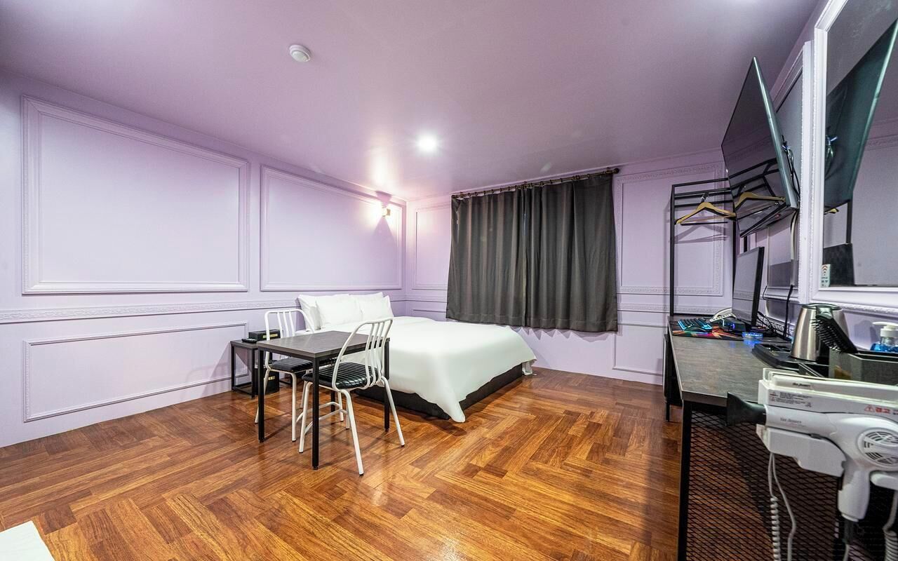 A hotel room with a bed, a desk with a computer, a chair, and a hairdryer.