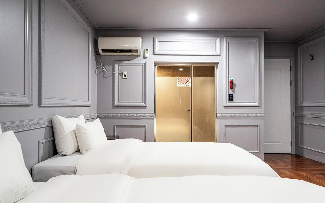 A hotel room with a bed, a wardrobe, an air conditioning unit, and an elevator.