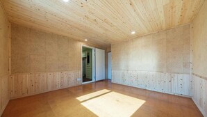 Ein geräumiges Zimmer mit holzgetäfelten Wänden und Decke, einem großen Holzboden und einer Tür zu einem weiteren Raum.