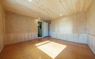 Una habitación amplia con paredes y techo de paneles de madera, un piso de madera grande y un acceso a otra habitación.