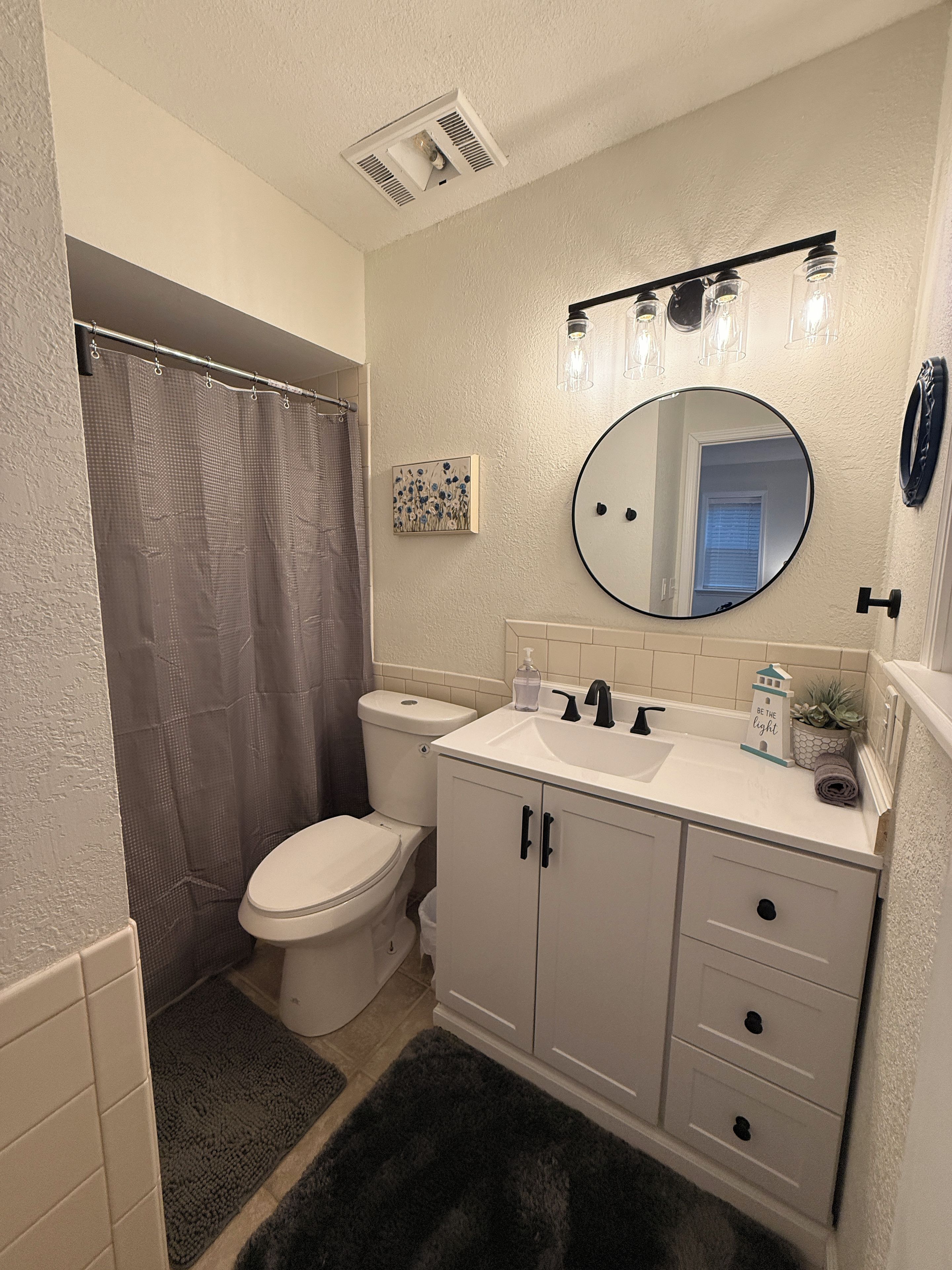 Baño con inodoro, lavamanos, espejo y cortina de ducha.