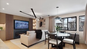 A modern living room with a fireplace, a TV, and a dining area with a table and chairs. - Ski-In Aspen Retreat Next To Lift 1A with Fireplace & Walkable Downtown Access (Aspen)