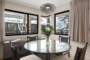 A round glass table with chairs, a vase with flowers, and a view of snow-covered trees through large windows. - Ski-In Aspen Retreat Next To Lift 1A with Fireplace & Walkable Downtown Access (Aspen)