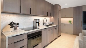 A modern kitchen with dark wood cabinets, a marble countertop, and built-in appliances. - Ski-In Aspen Retreat Next To Lift 1A with Fireplace & Walkable Downtown Access (Aspen)