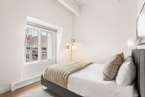 Ein Schlafzimmer mit einem Bett, einem Fenster, einer Wandleuchte und einer Heizung.