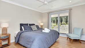 A bedroom with a bed, bedside lamps, a chair, and a view of trees through a glass door. - Shiraz Vineyard Estate (Pokolbin)