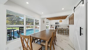 Una cocina moderna con armarios blancos, una mesa de comedor de madera y vistas a una piscina.